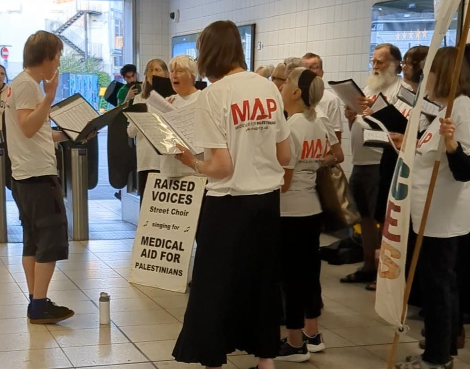 Raised Voices singing at MAP busking, Jake conducts