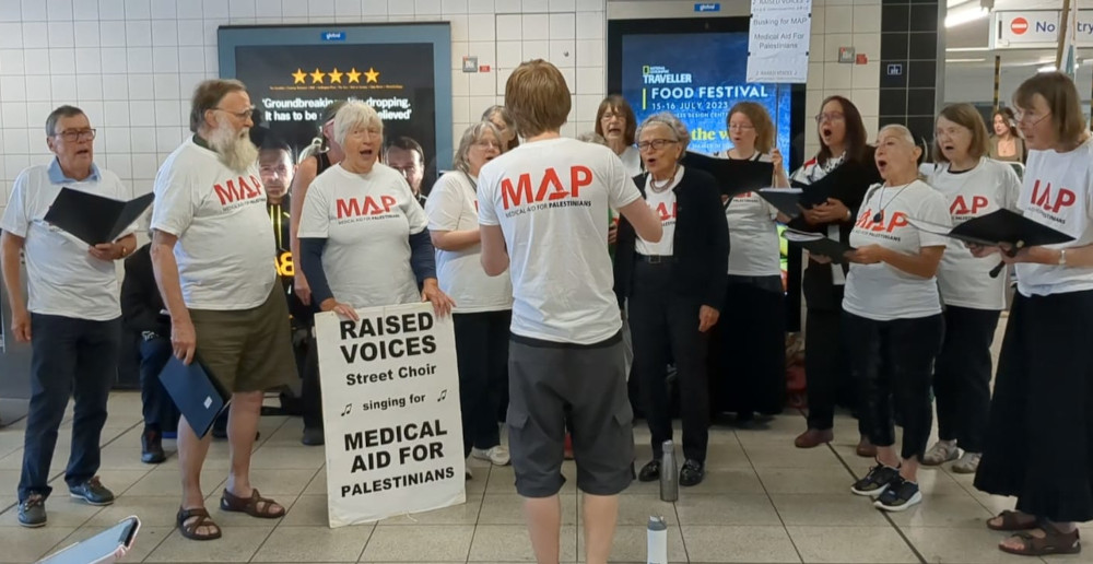 Raised Voices singing at MAP busking, Jake conducts